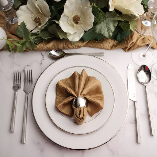 Elegant table setting with gold napkin, silverware, and floral centerpiece on a marble surface.